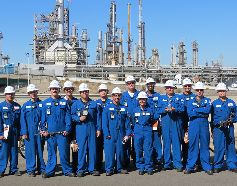 Operators in blue nomex grouped for a photo in front of refinery