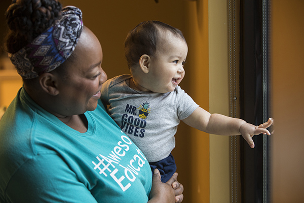 A Valero Family Center caregiver holds an infant to look out of a window