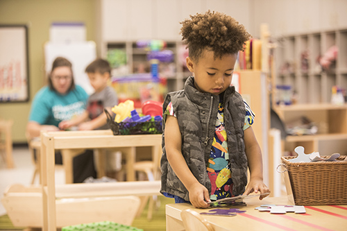 Small child playing in a daycare facility, with teacher in the background.