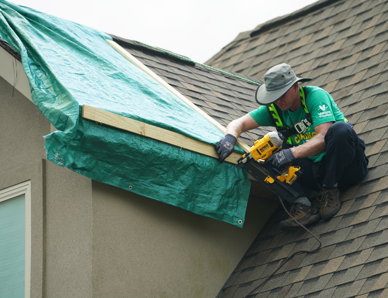Valero volunteer on top of a home's roof fixing damages