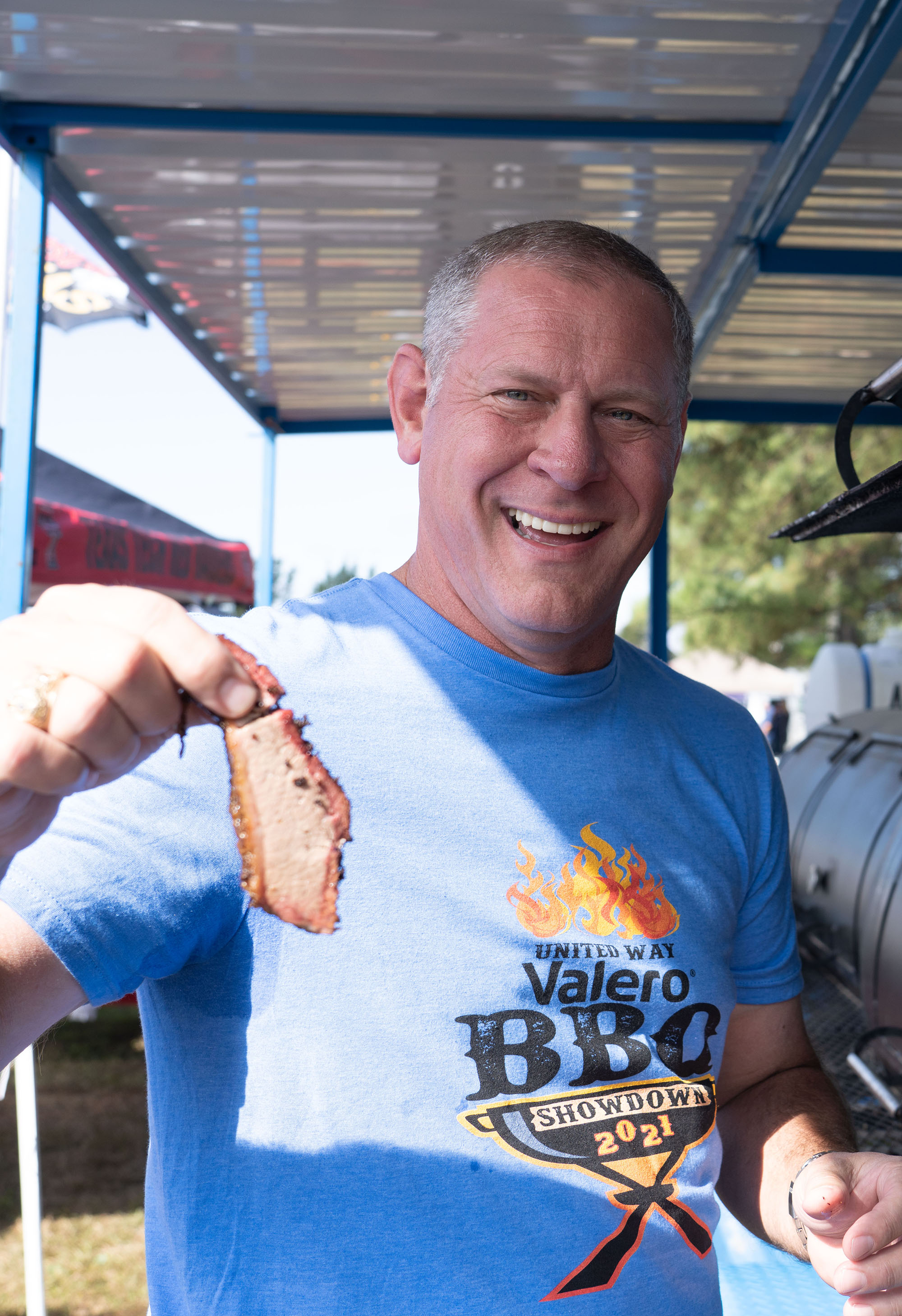 Man holds piece of brisket and smiles