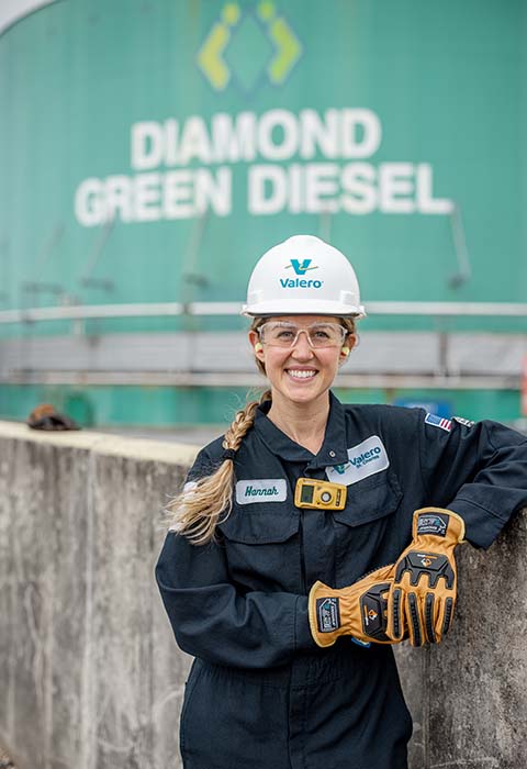 A woman in fire protective clothing and a Valero-branded hard hat stands in front of the Diamond Green Diesel logo.
