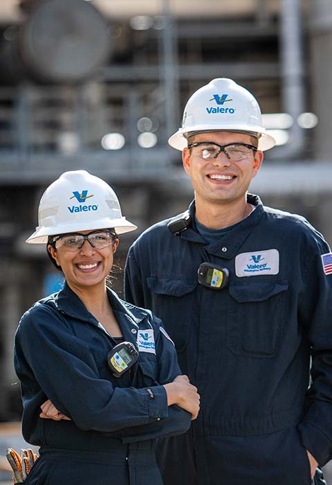 Two Valero refinery employees stand and smile in front of equipment.