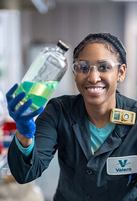 A Valero engineer smiles and holds lab equipment.