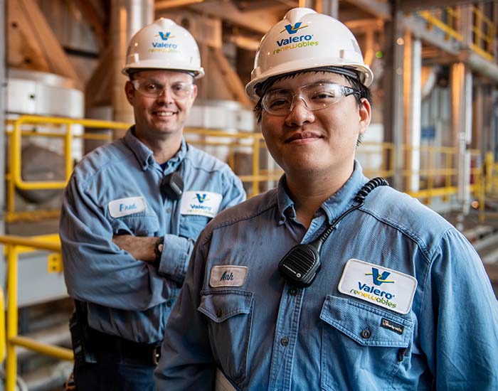 Two Valero employees stand together and smile in front of equipment.