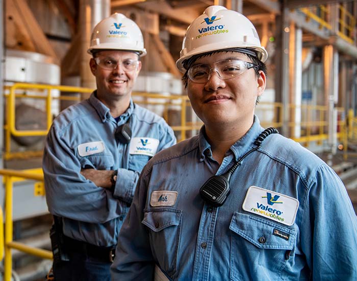 Two Valero employees stand together and smile in front of equipment.
