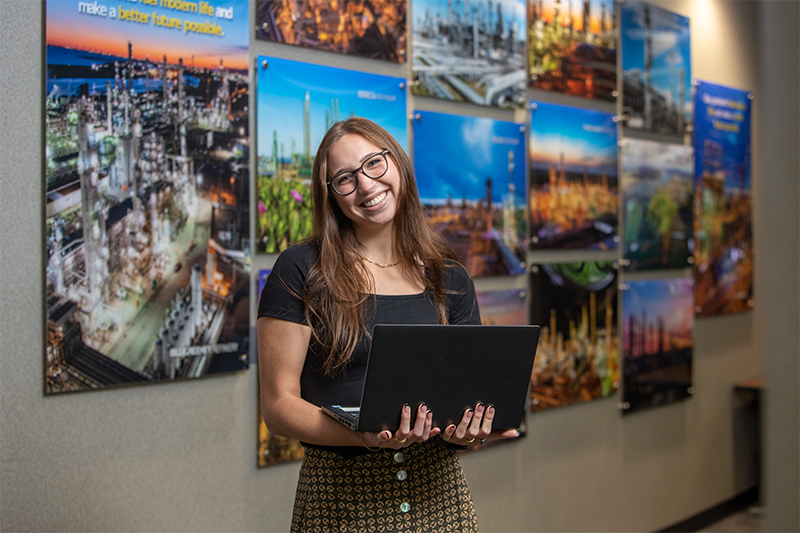 Media Intern standing smiling while holding laptop.