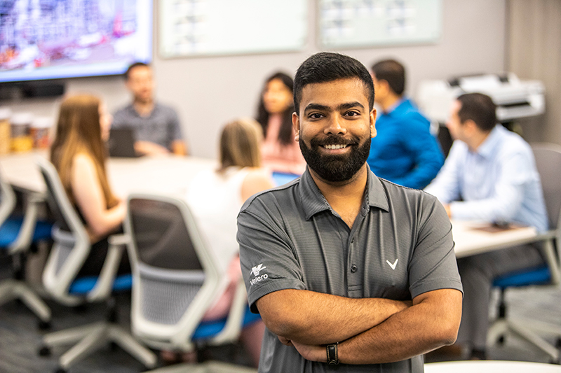 Employee posed smiling with group of employees meeting in the background