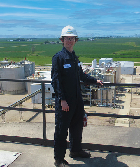 Intern standing on structure with greenery in the background.