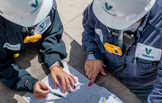 Two Valero employees in full PPE are at a refinery and reviewing schematics.