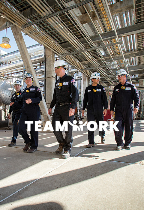 Valero employees wearing full PPE walk together at a refinery. Text reads: Teamwork.