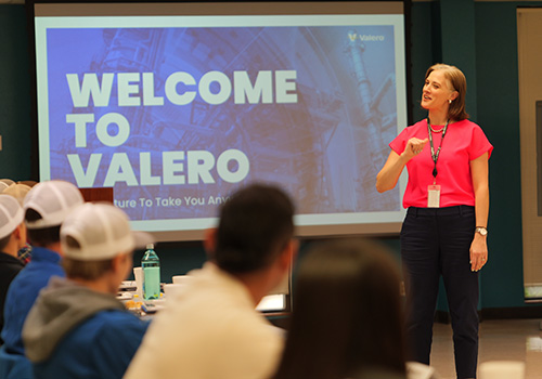 A Valero BOT Training session. A female instructor stands before seated trainees in front of a screen reading "Welcome to Valero."
