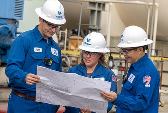 Operators working together, reviewing refinery plans near a refining unit.
