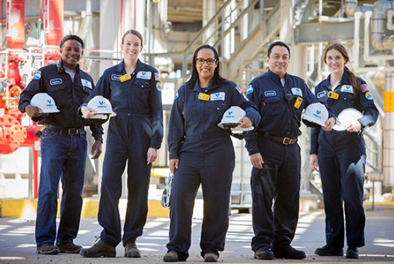 5 Refinery Engineers standing in a refinery holding their helmets