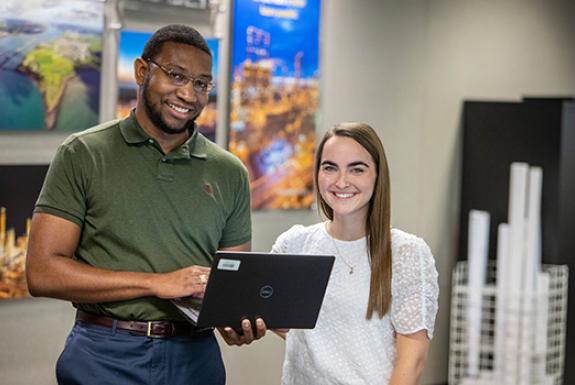 Two individuals, one holding laptop, smiling at camera