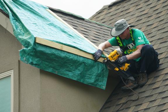Valero volunteer on top of a home's roof fixing damages