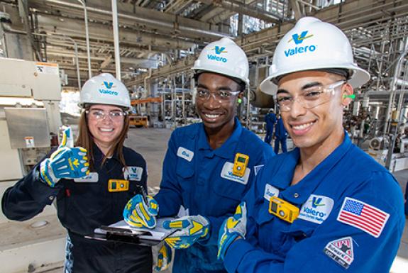 Valero interns wearing hard hats and PPE smile while working together at the Valero Corpus Christi refinery.
