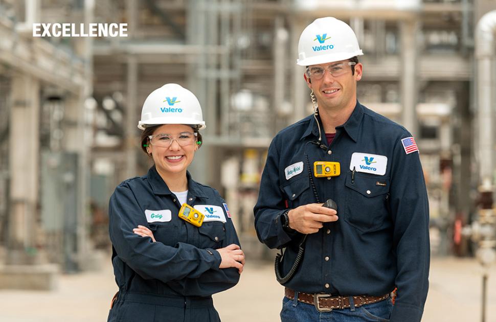 Two operators pose looking proudly in front of a refining unit