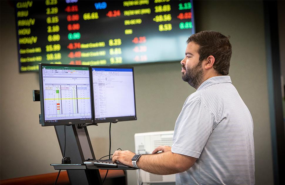 Male working on computer with TV of stock prices in the background