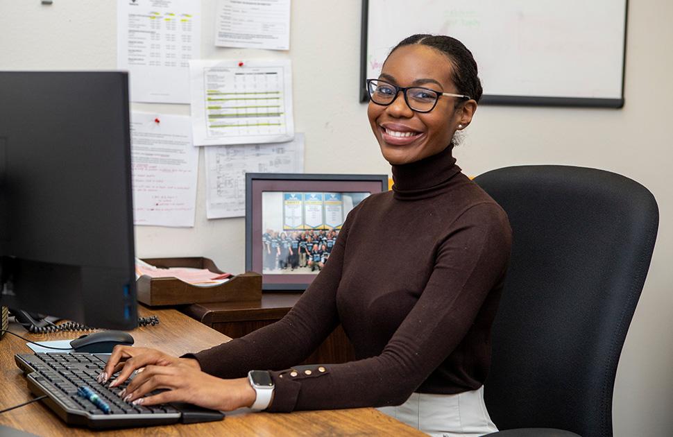 Woman on computer, looking and smiling at camera