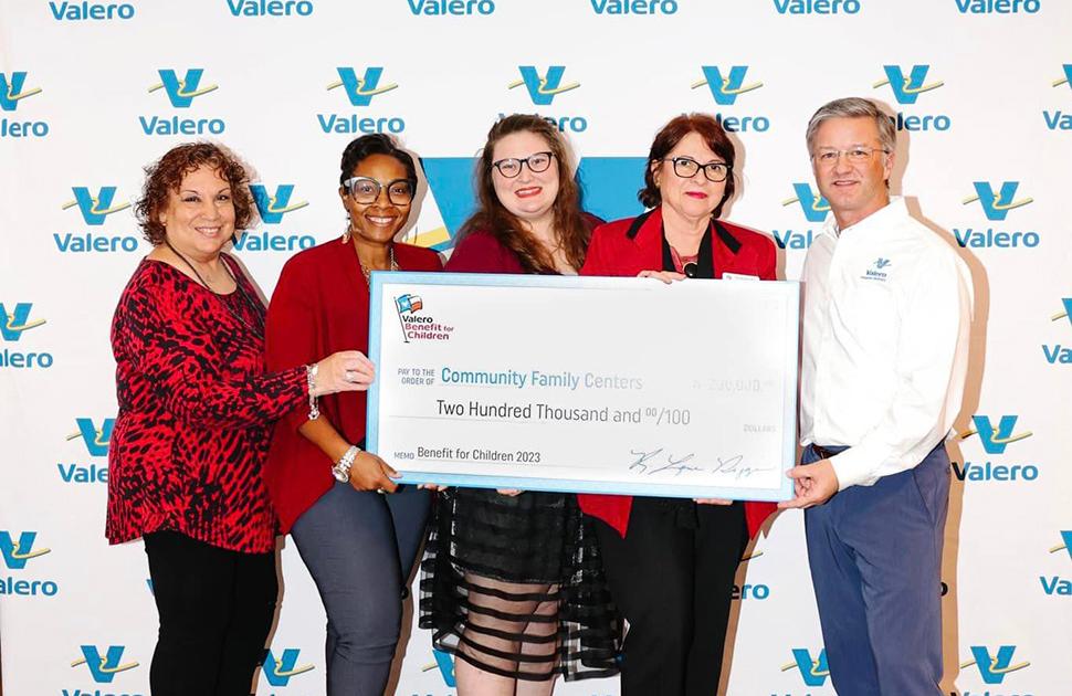 Five people stand in front of a Valero-decorated background and are holding an oversized check for a $200k donation to Community Family Centers