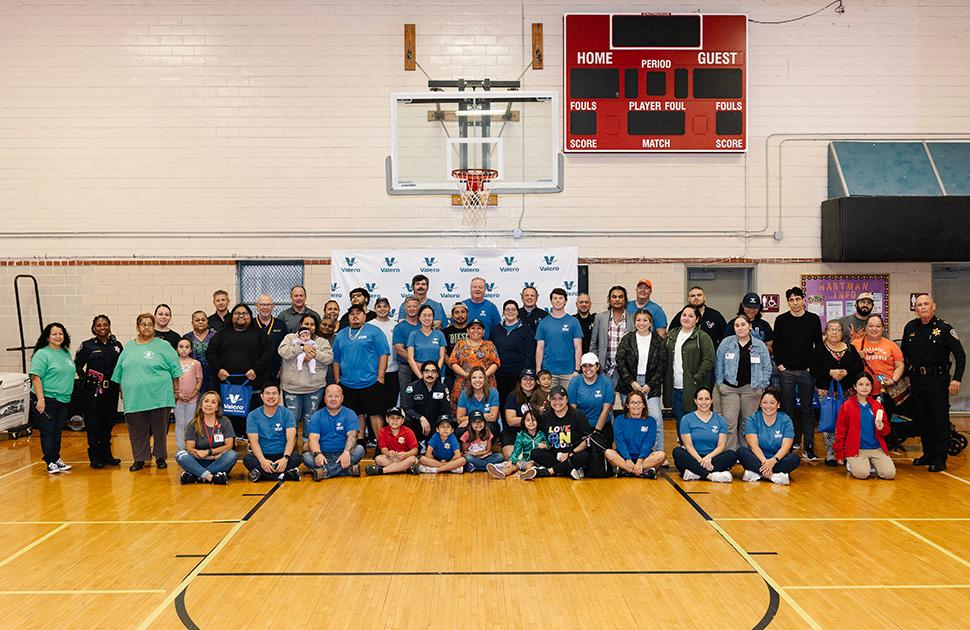 Valero volunteers pose together for a photo beneath a basketball hoop inside a gymnasium.