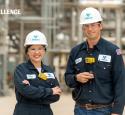 Two operators pose looking proudly in front of a refining unit