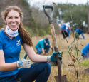 Volunteer smiles while holding a shovel, planting trees.