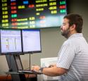 Male working on computer with TV of stock prices in the background