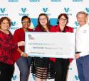 Five people stand in front of a Valero-decorated background and are holding an oversized check for a $200k donation to Community Family Centers