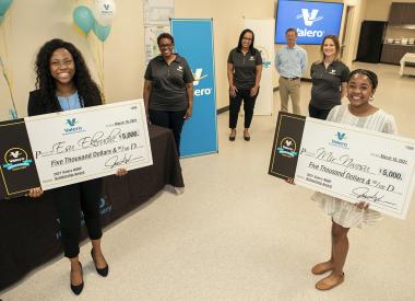 Girls smile with their NSBE scholarship checks, Valero reps smile in background